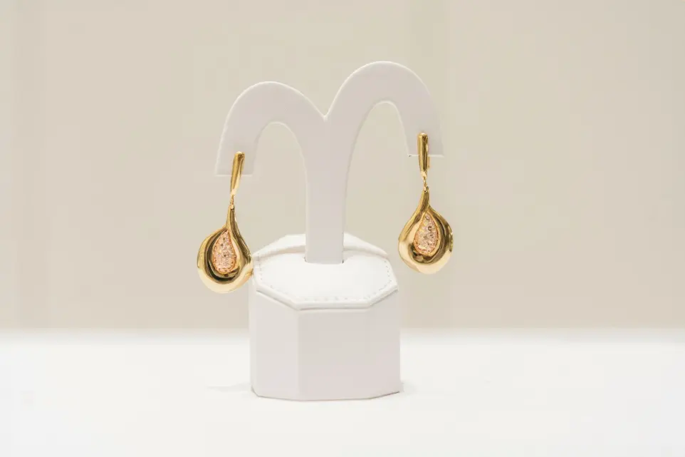 a pair of gold and diamond earrings on a white stand